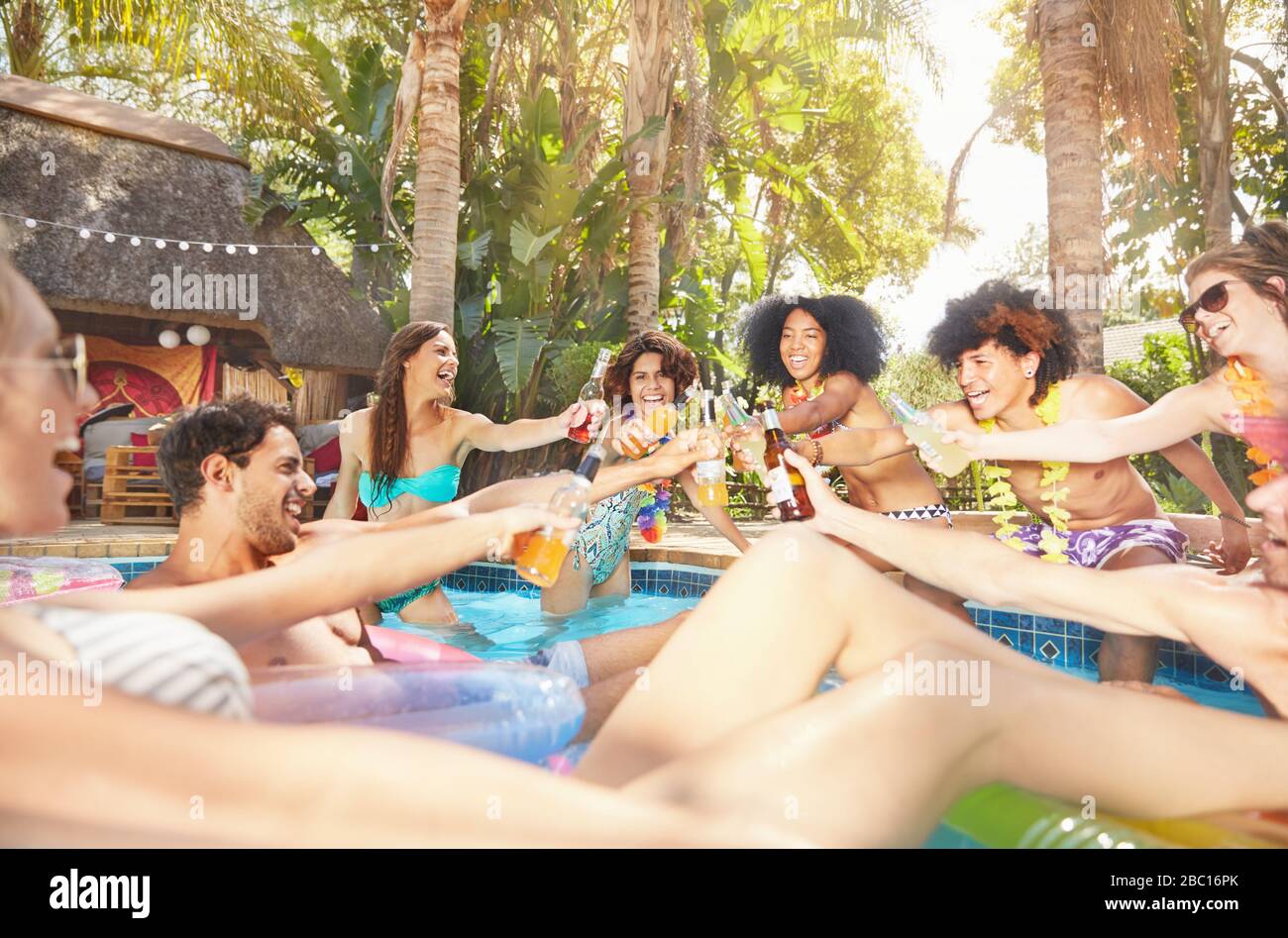 Amici entusiasti che bevono, tostano bottiglie di birra e cocktail durante la festa estiva in piscina Foto Stock