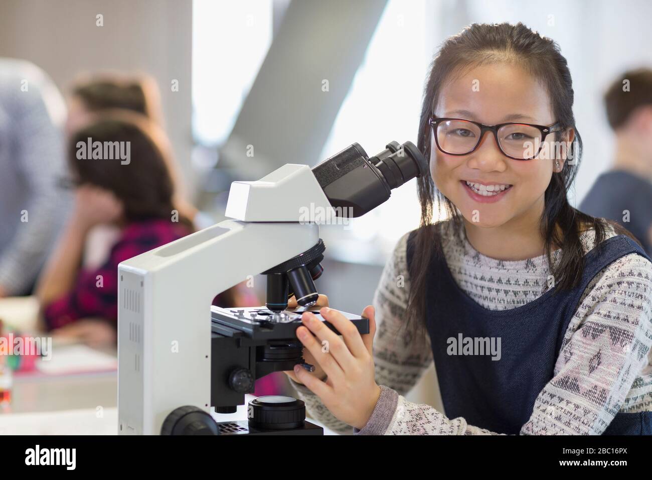 Ritratto sorridente, ragazza sicura studente al microscopio, condurre esperimenti scientifici in classe di laboratorio Foto Stock