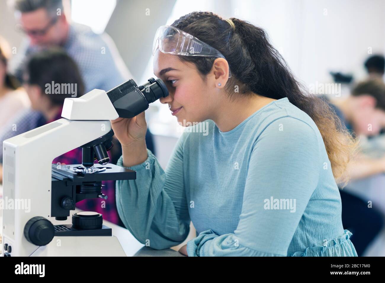 Studentessa studentesca al microscopio, conducendo esperimenti scientifici in classe di laboratorio Foto Stock