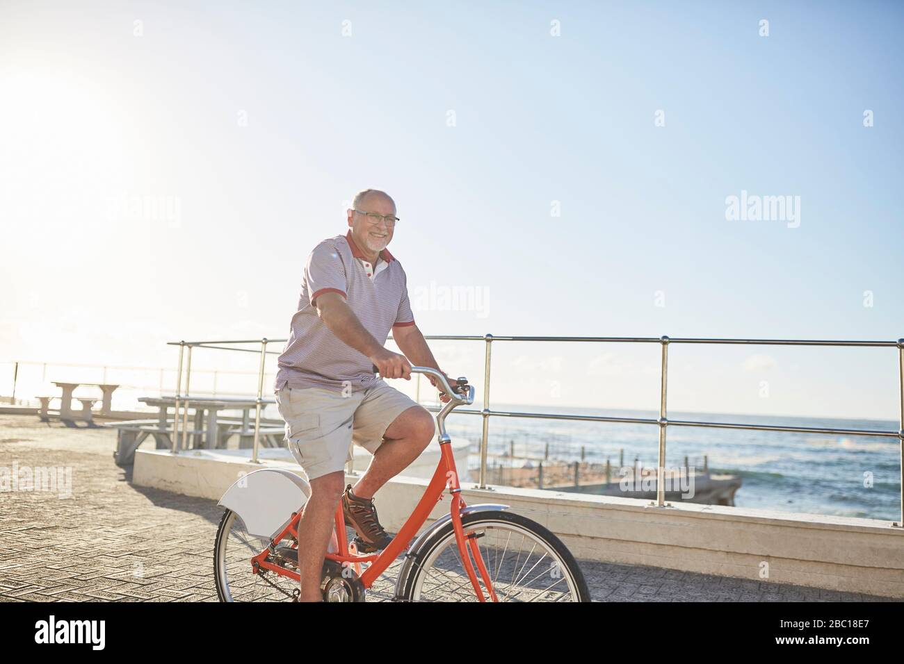 Uomo anziano attivo in bicicletta turistica a cavallo sul lungomare soleggiato lungo l'oceano Foto Stock