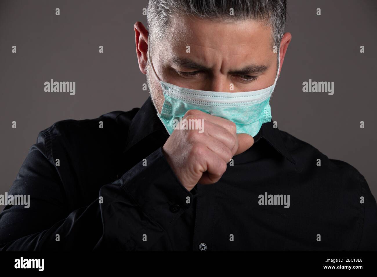 Ritratto chiuso dell'uomo con maschera chirurgica che tossisce in studio su sfondo grigio, concetto sanitario. Foto Stock