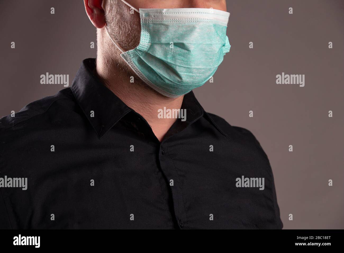 Ritratto di un uomo con maschera di protezione chirurgica su sfondo grigio. Concetto di coronavirus. Proteggere la salute. Foto Stock