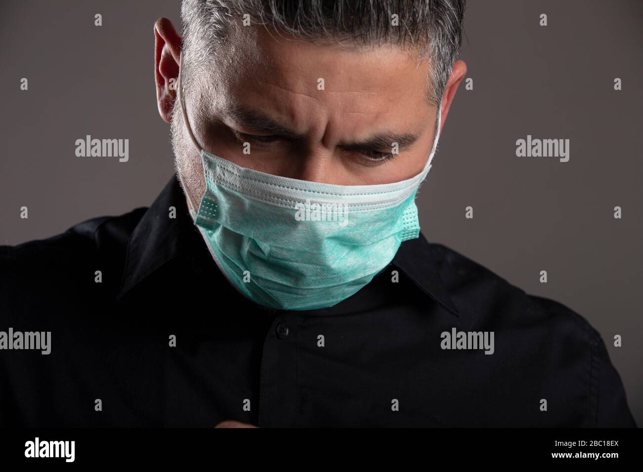 Ritratto di uomo downcast con maschera di protezione medica su sfondo grigio studio. Concetto di quarantena del coronavirus. Foto Stock