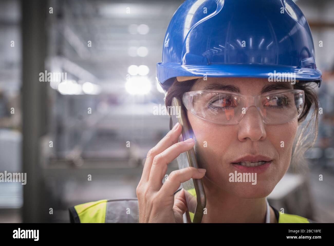 Primo piano: Donna che parla con lo smartphone in fabbrica Foto Stock