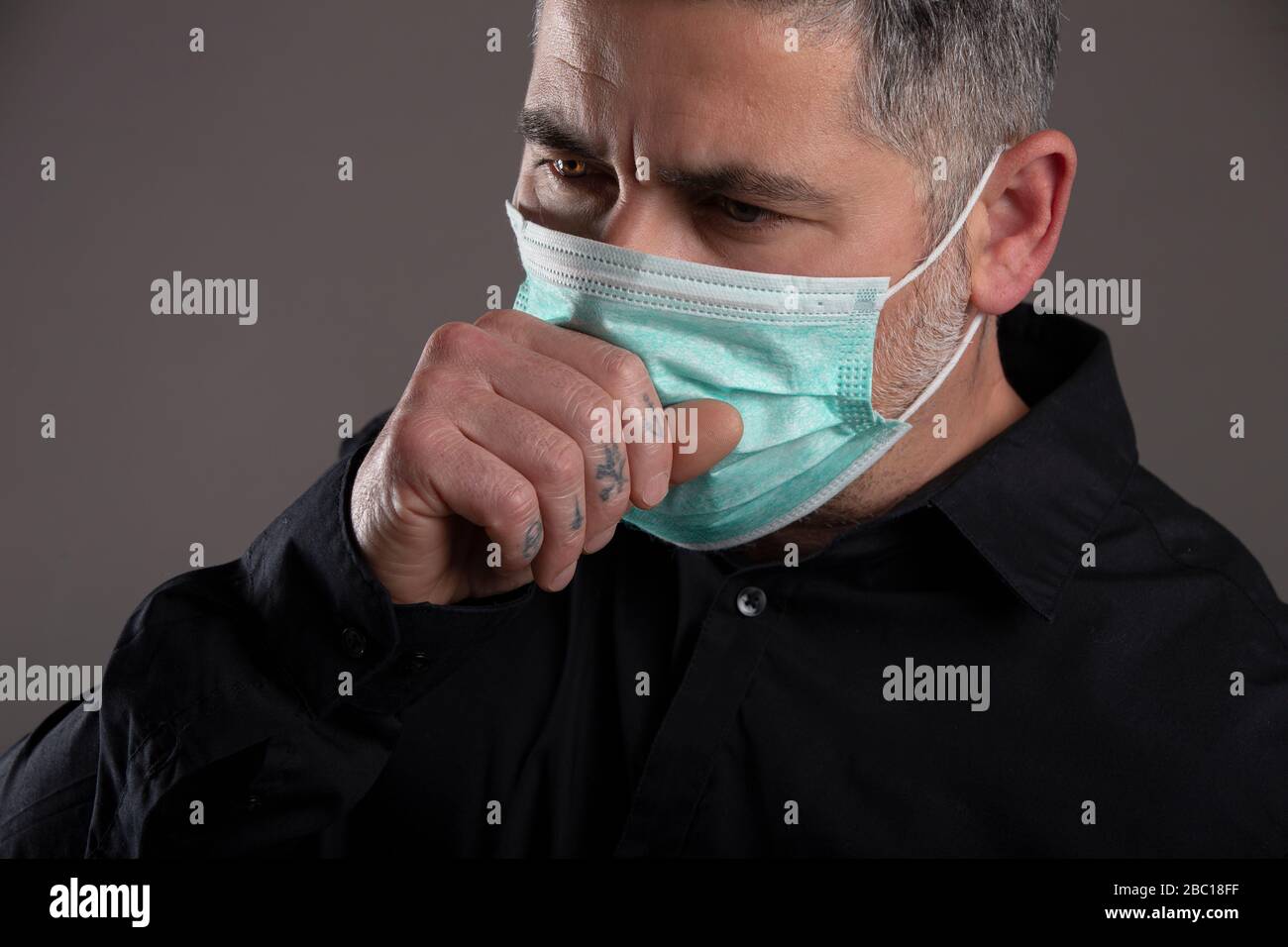 Primo piano dell'uomo con maschera chirurgica che tossisce su sfondo grigio, concetto sanitario. Coronavirus Foto Stock
