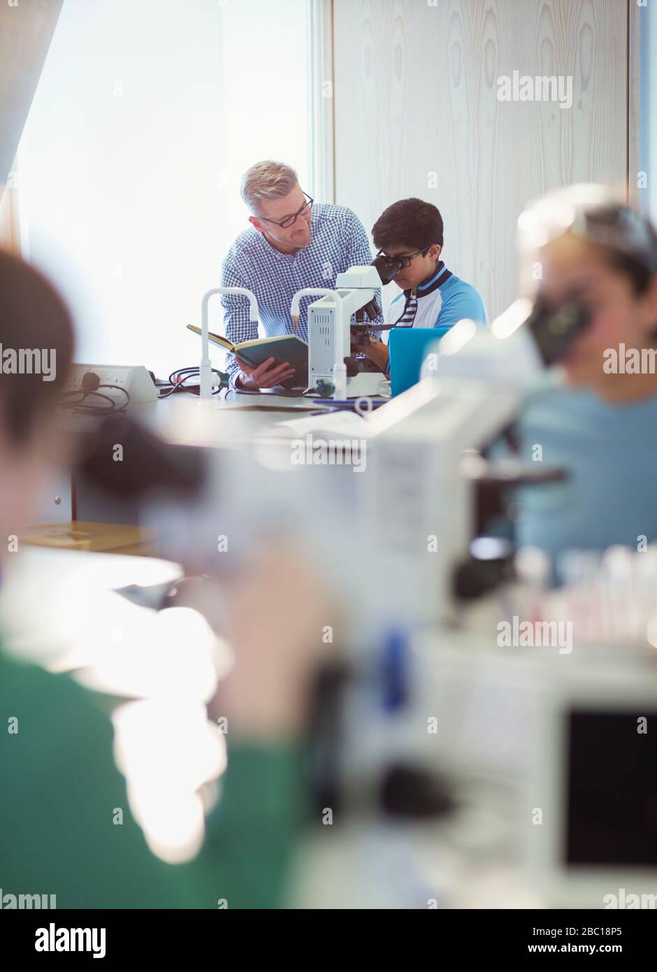 Insegnante di sesso maschile e studente di ragazzo al microscopio, conducendo esperimenti scientifici in classe di laboratorio Foto Stock