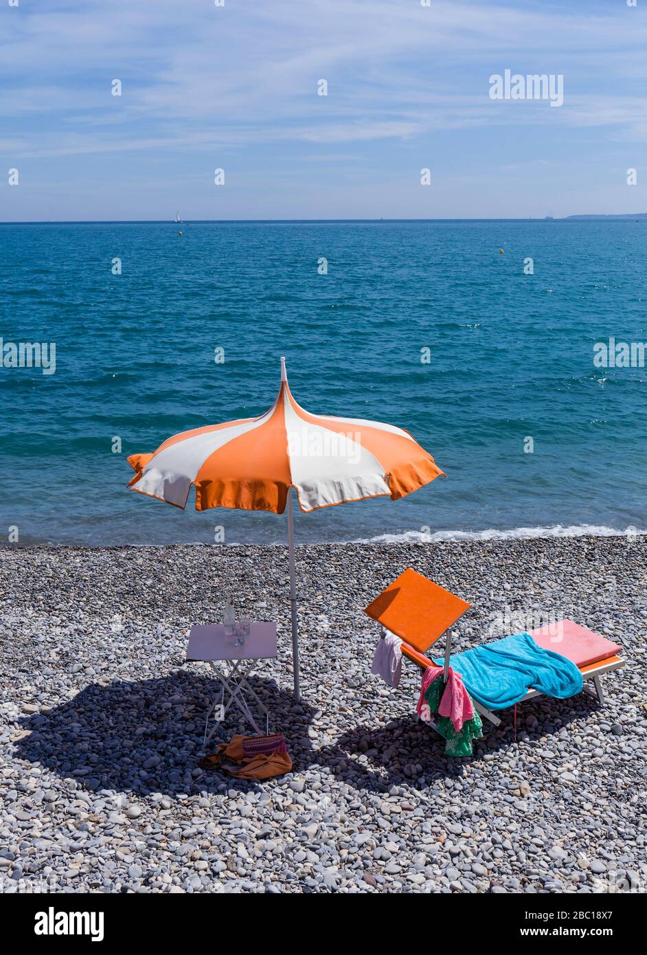 Francia, Alpes-Maritimes, Cagnes-sur-Mer, ombrellone e sdraio sulla spiaggia costiera rocciosa con linea di orizzonte sul Mar Mediterraneo sullo sfondo Foto Stock
