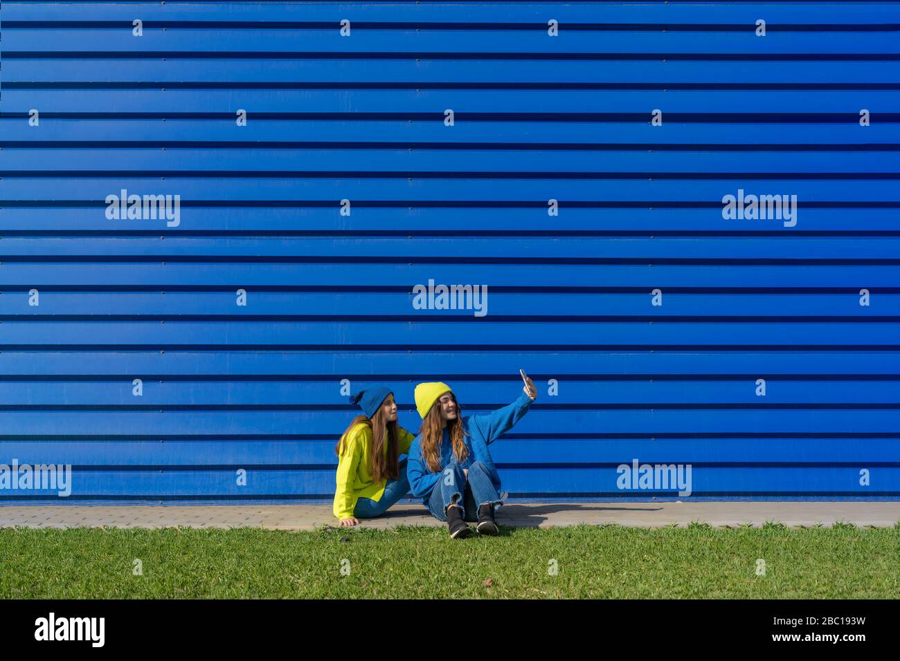 Due ragazze adolescenti che indossano abiti abbinati che portano selfie con smartphone davanti a sfondo blu Foto Stock