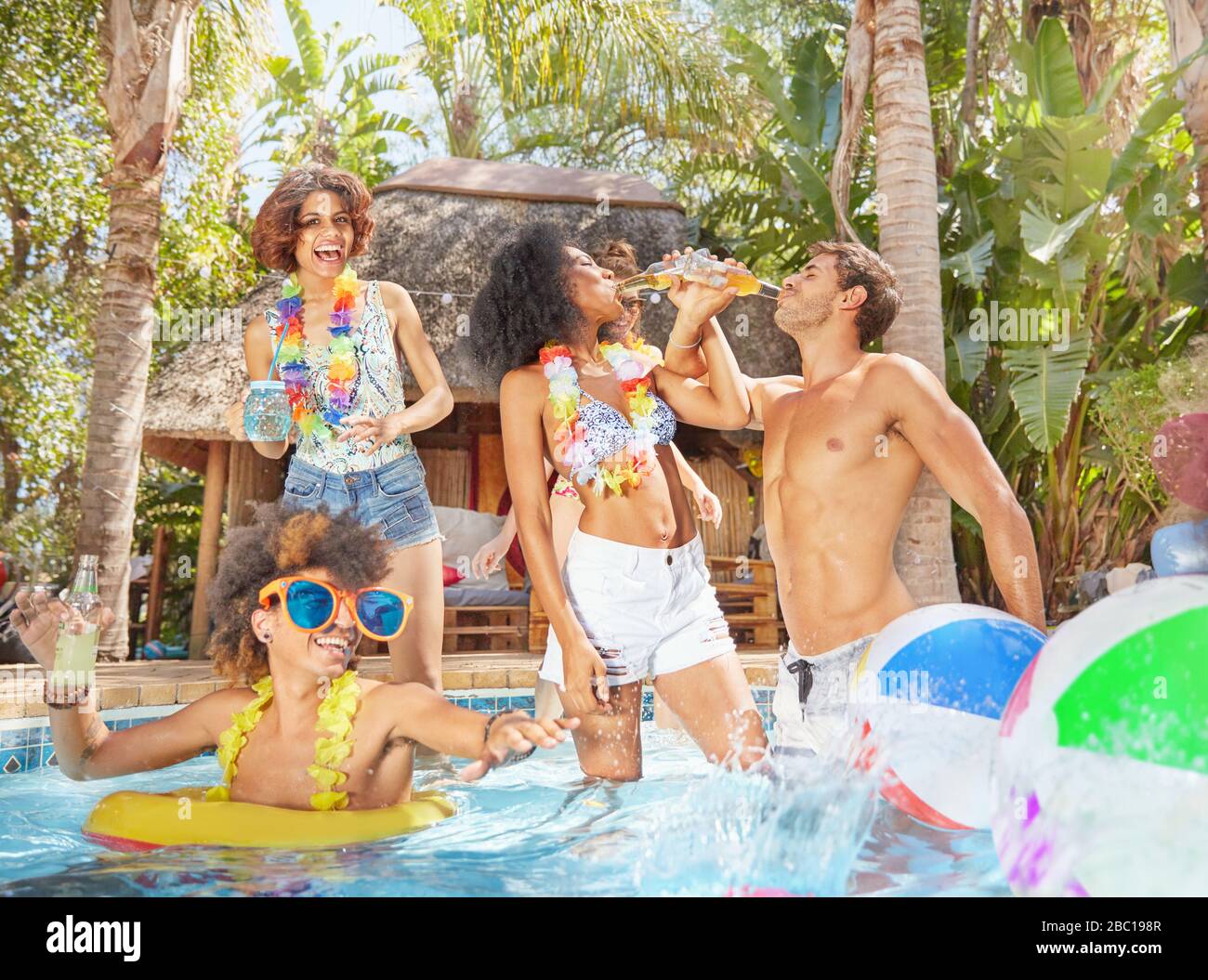 Giocosi giovani amici che bevono e giocano nella soleggiata piscina estiva Foto Stock