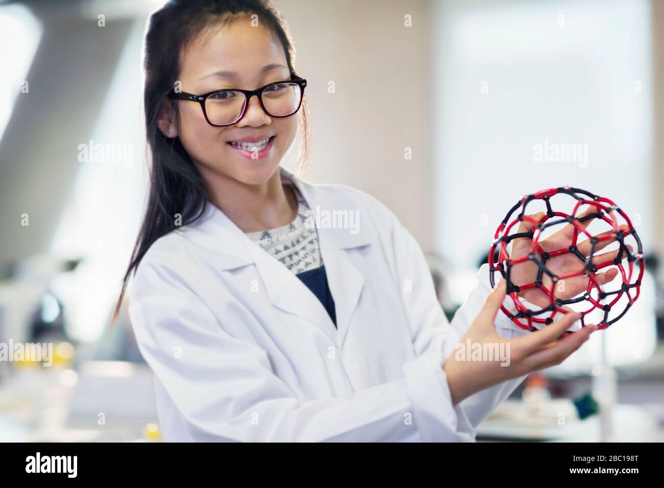 Ritratto sorridente, sicura studentessa in possesso di struttura molecolare in classe di laboratorio Foto Stock