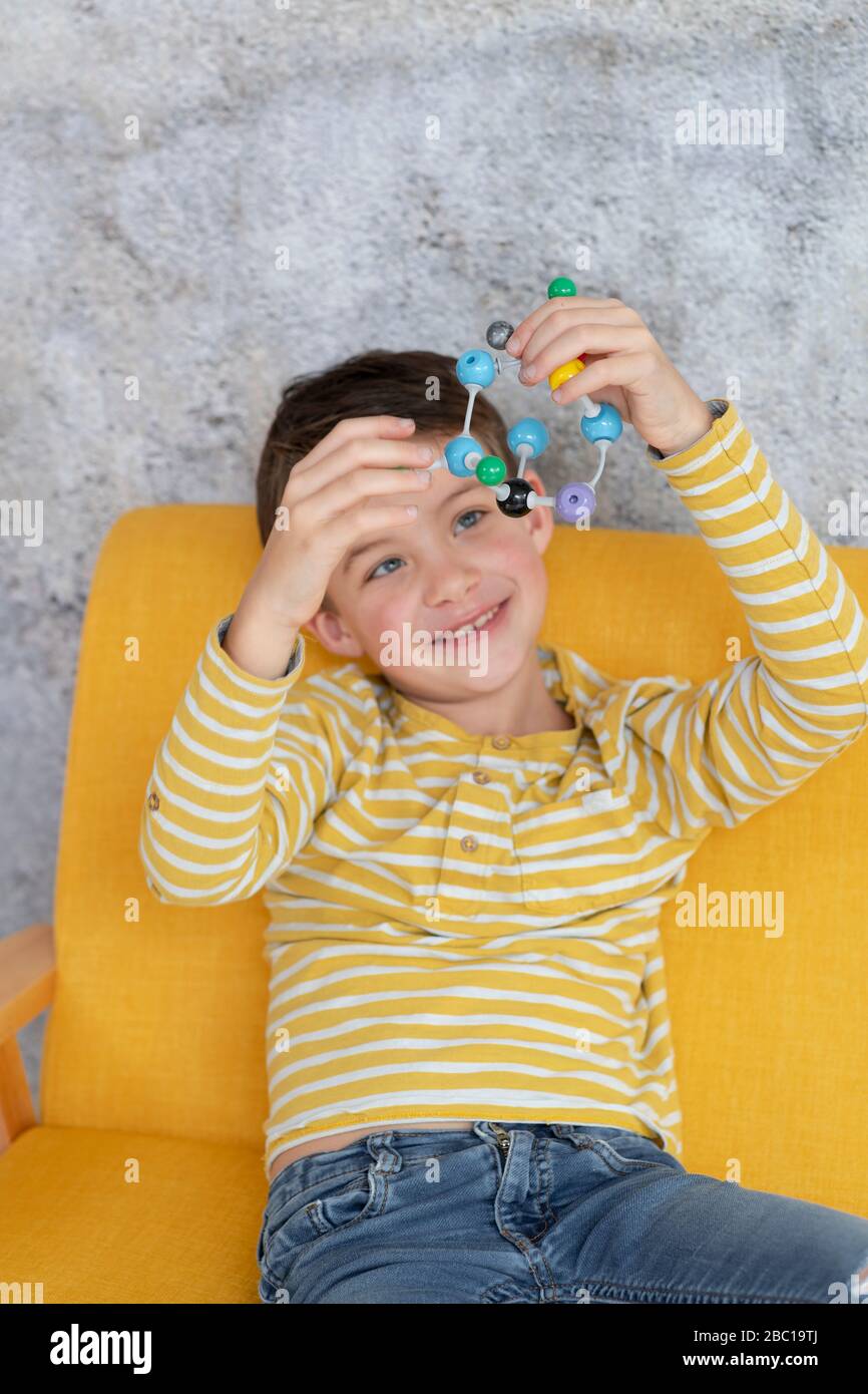 Ragazzo sta giocando e sperimentando con modelli molecolari seduti su un divano giallo Foto Stock