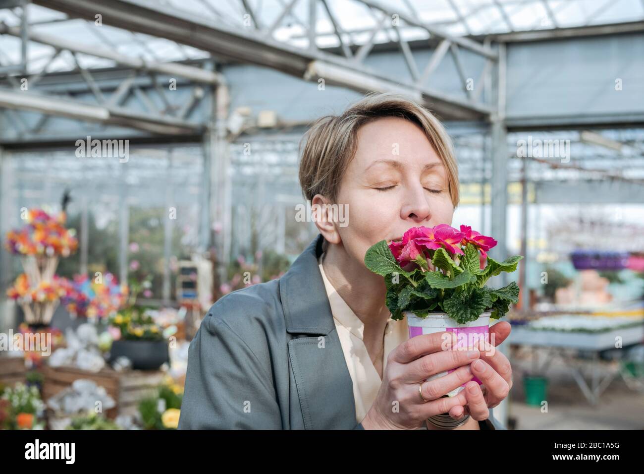Donna con occhi chiusi che sniffing fiori rosa in negozio di fiori Foto Stock