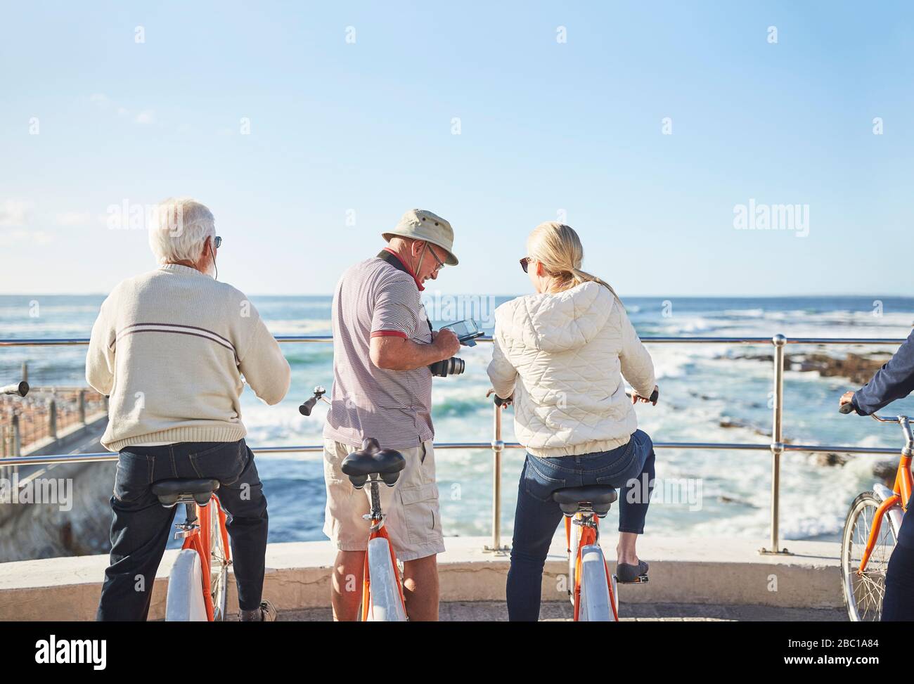 Turisti anziani attivi in bicicletta che guardano all'oceano soleggiato vista Foto Stock