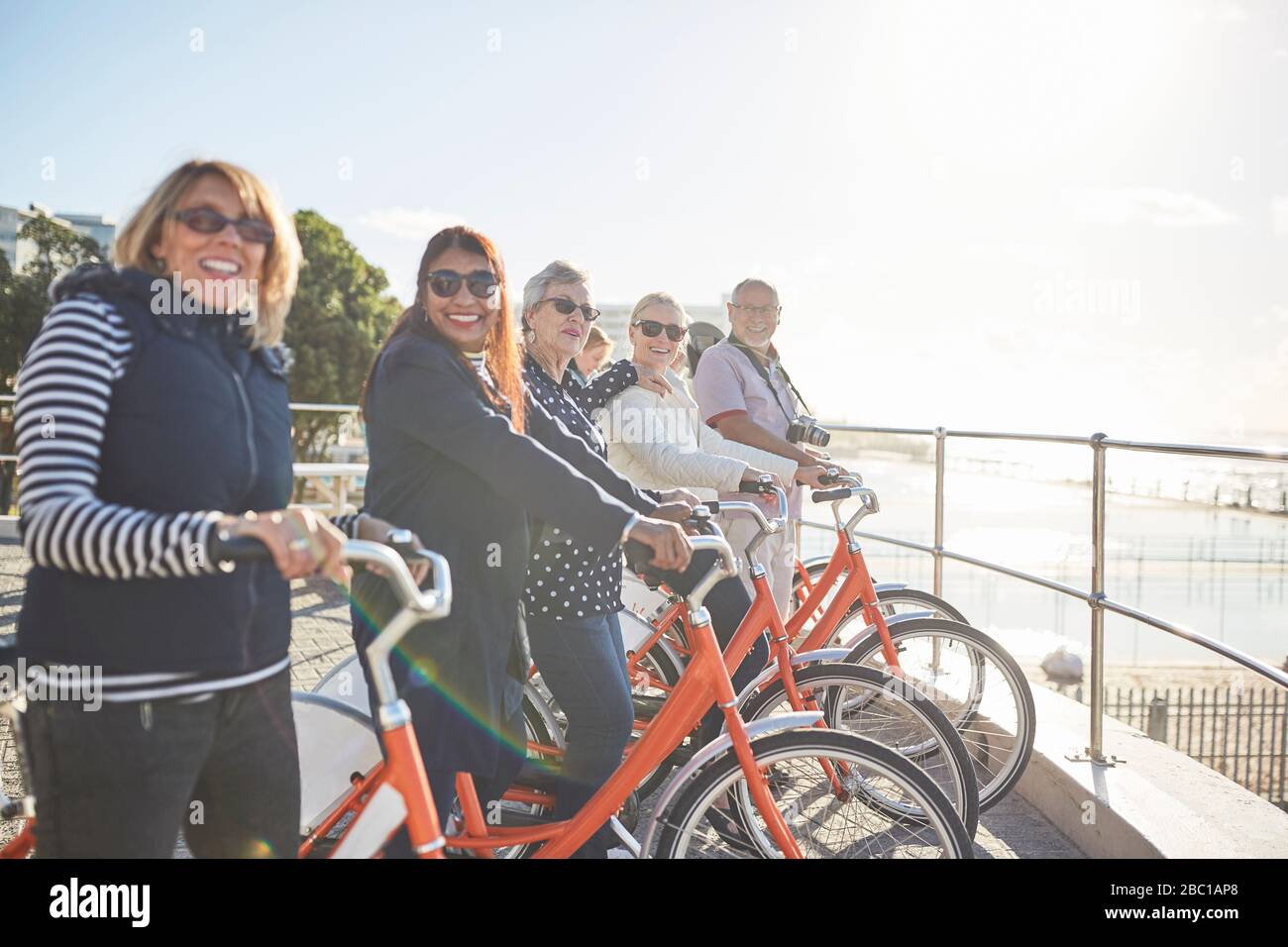 Ritratto sorridente, fiducioso attivo senior turistico amici in bicicletta sul lungomare soleggiato Foto Stock