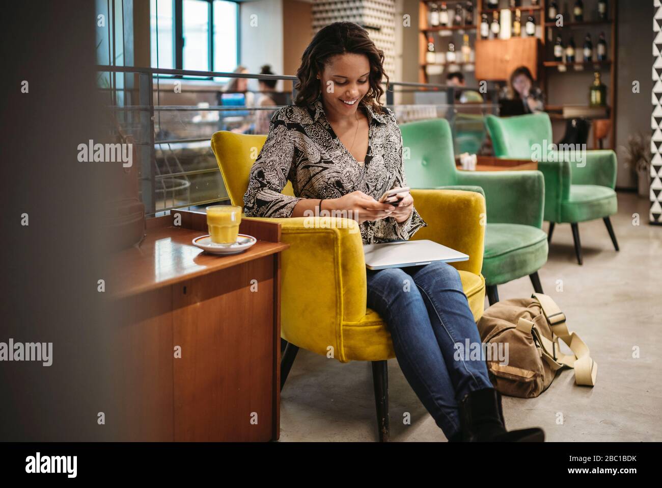 Giovane donna seduta in poltrona con computer portatile e smartphone Foto Stock