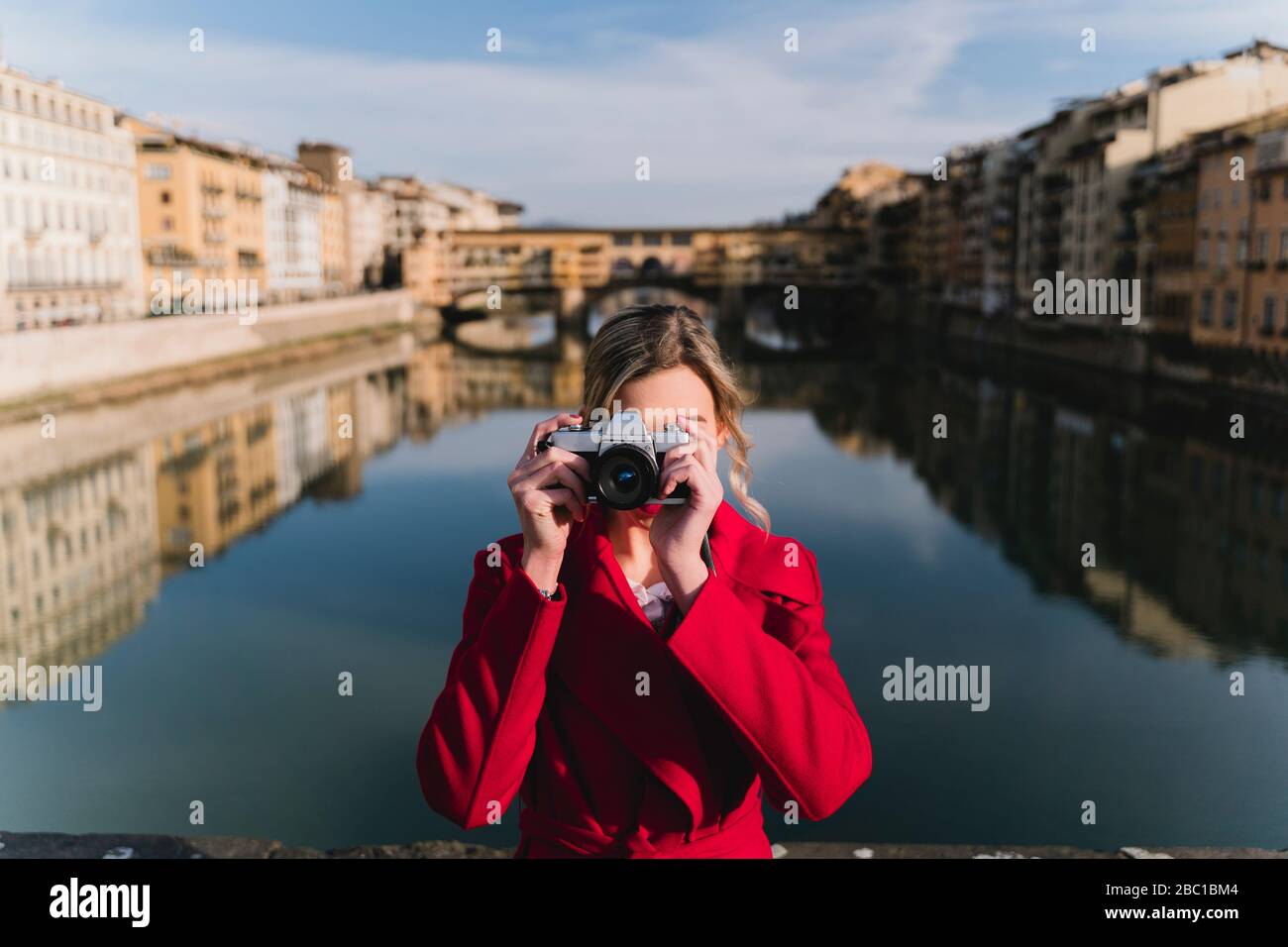 Giovane donna che prende una foto su un ponte sopra il fiume Arno, Firenze, Italia Foto Stock