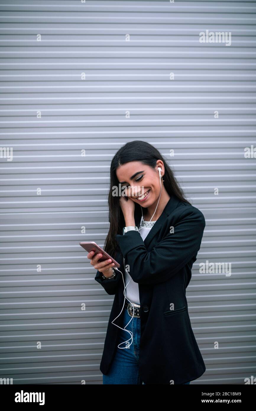 Ritratto di giovane donna felice con smartphone che mette sugli auricolari Foto Stock