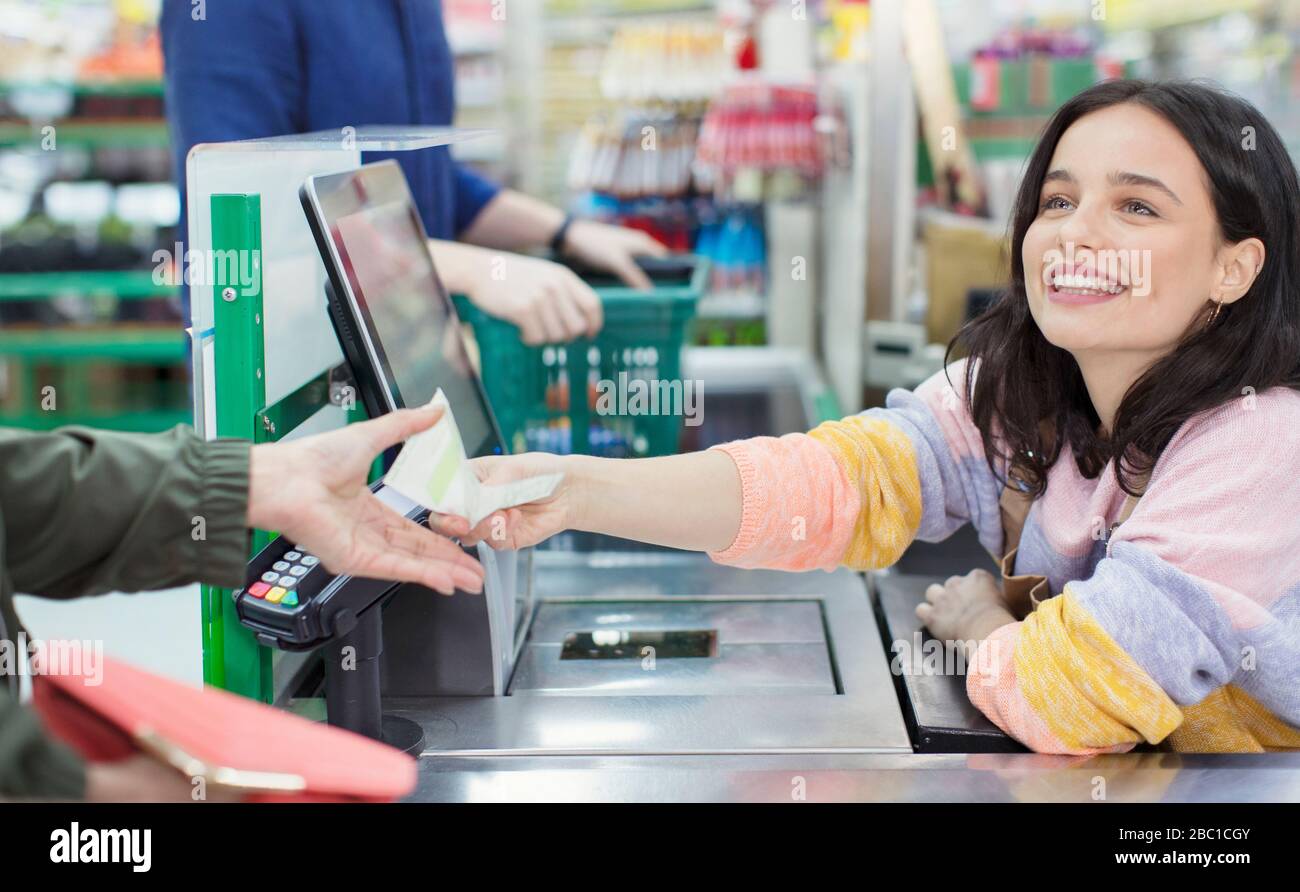 Cassiera sorridente che dà ricevuta al cliente al checkout del supermercato Foto Stock