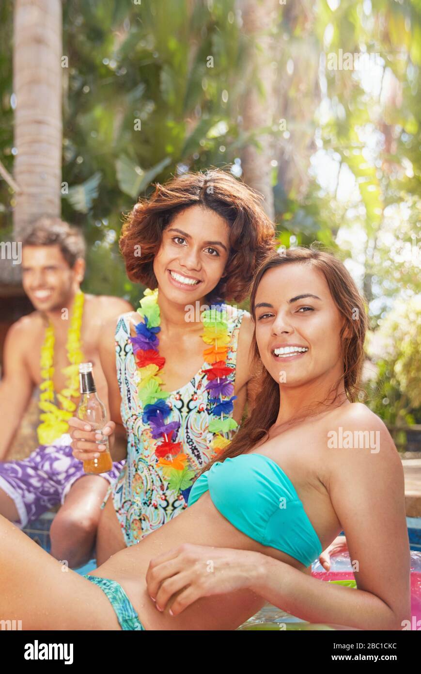 Ritratto sicuro, sorridente giovani donne amici appendere fuori, bere a bordo piscina Foto Stock