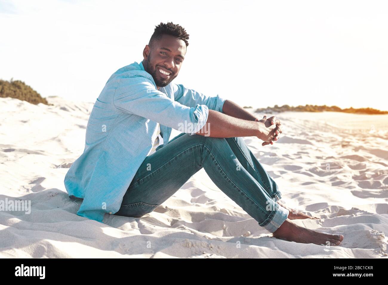 Ritratto sorridente, sicuro giovane uomo rilassante sulla spiaggia soleggiata estiva Foto Stock