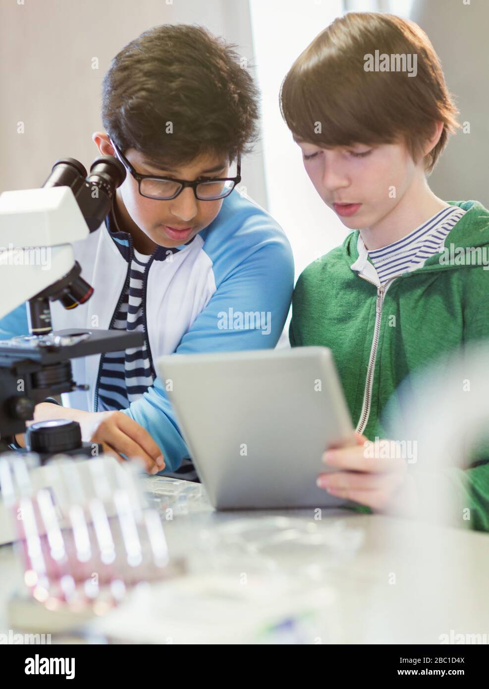 Studenti ragazzi concentrati utilizzando tablet e microscopio digitali, conducendo esperimenti scientifici in classe di laboratorio Foto Stock