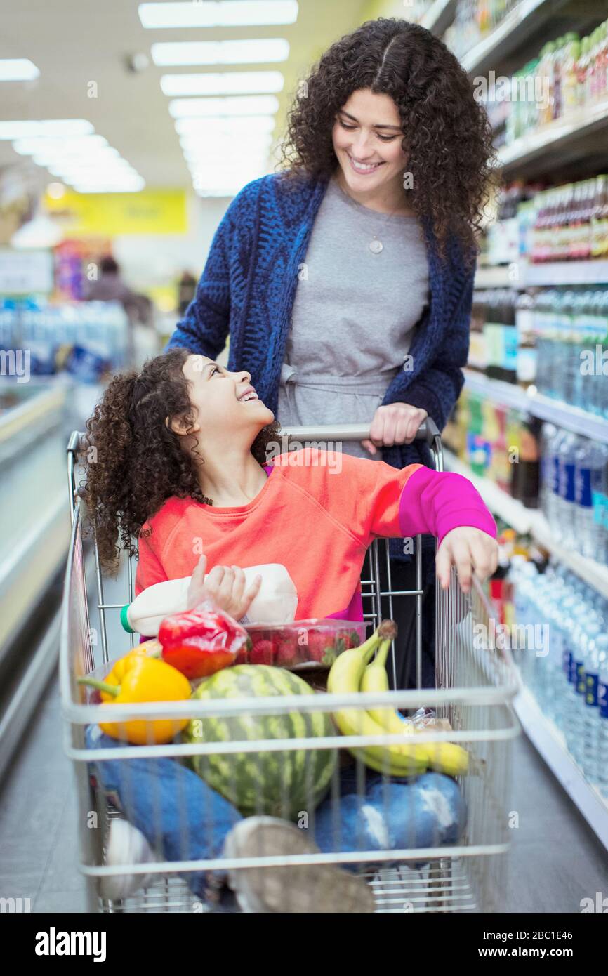 Madre felice che spinge la figlia nel carrello della spesa nel supermercato Foto Stock