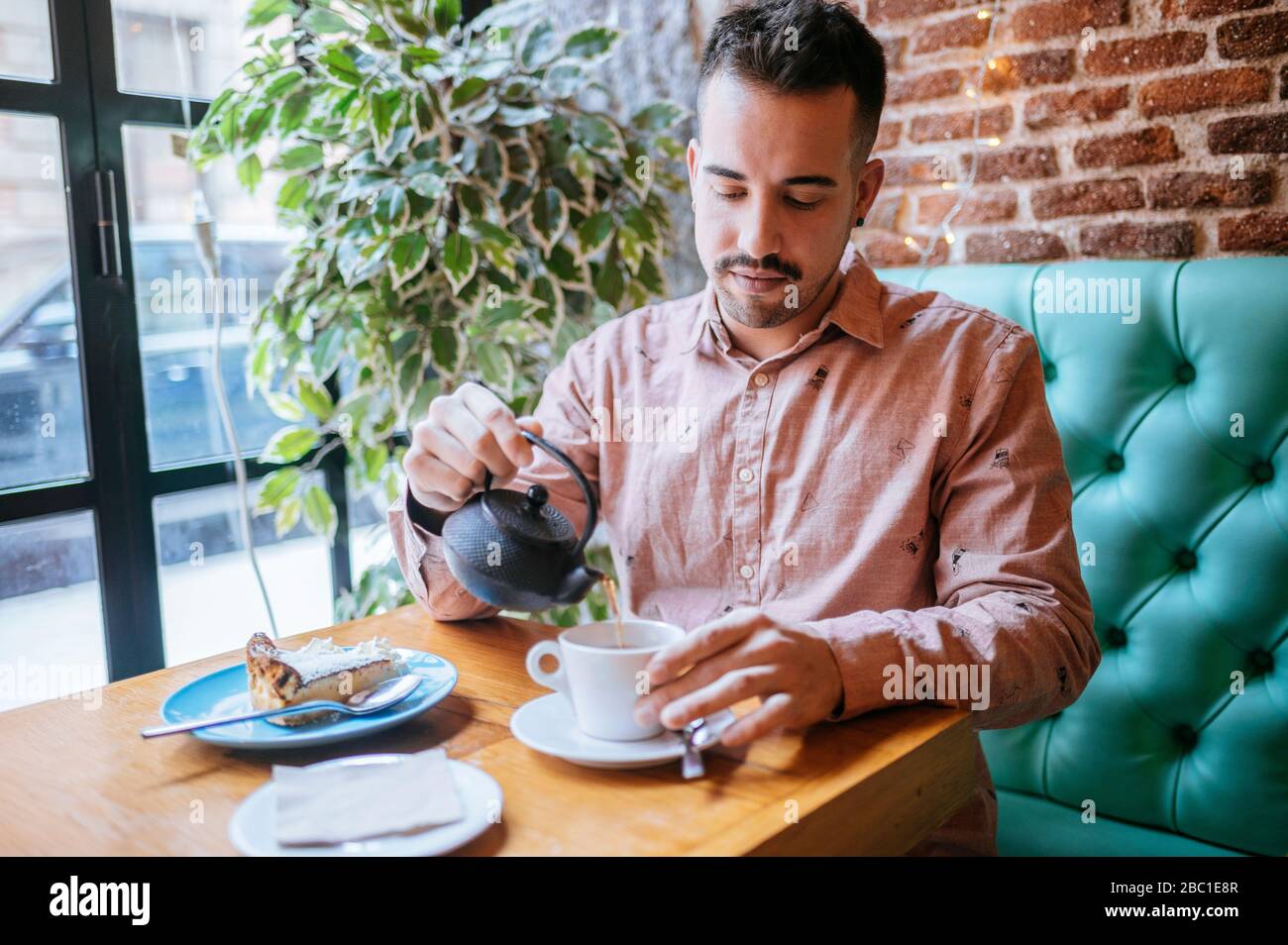 Uomo in un caffè che versa il tè in tazza Foto Stock