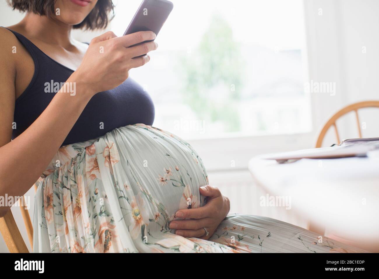 Donna incinta in abito floreale con smartphone Foto Stock