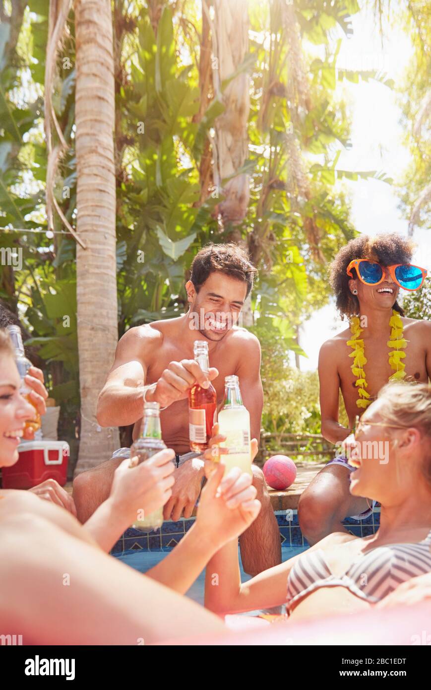 Giovani amici che si aggrappano, tostando le bottiglie di birra nella soleggiata piscina estiva Foto Stock