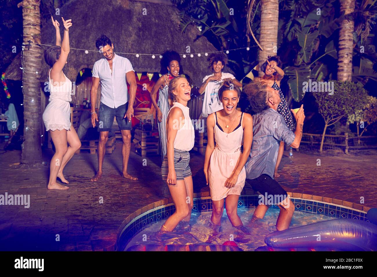 Giovani amici entusiasti che ballano e si aggrappano alla festa estiva a bordo piscina di notte Foto Stock