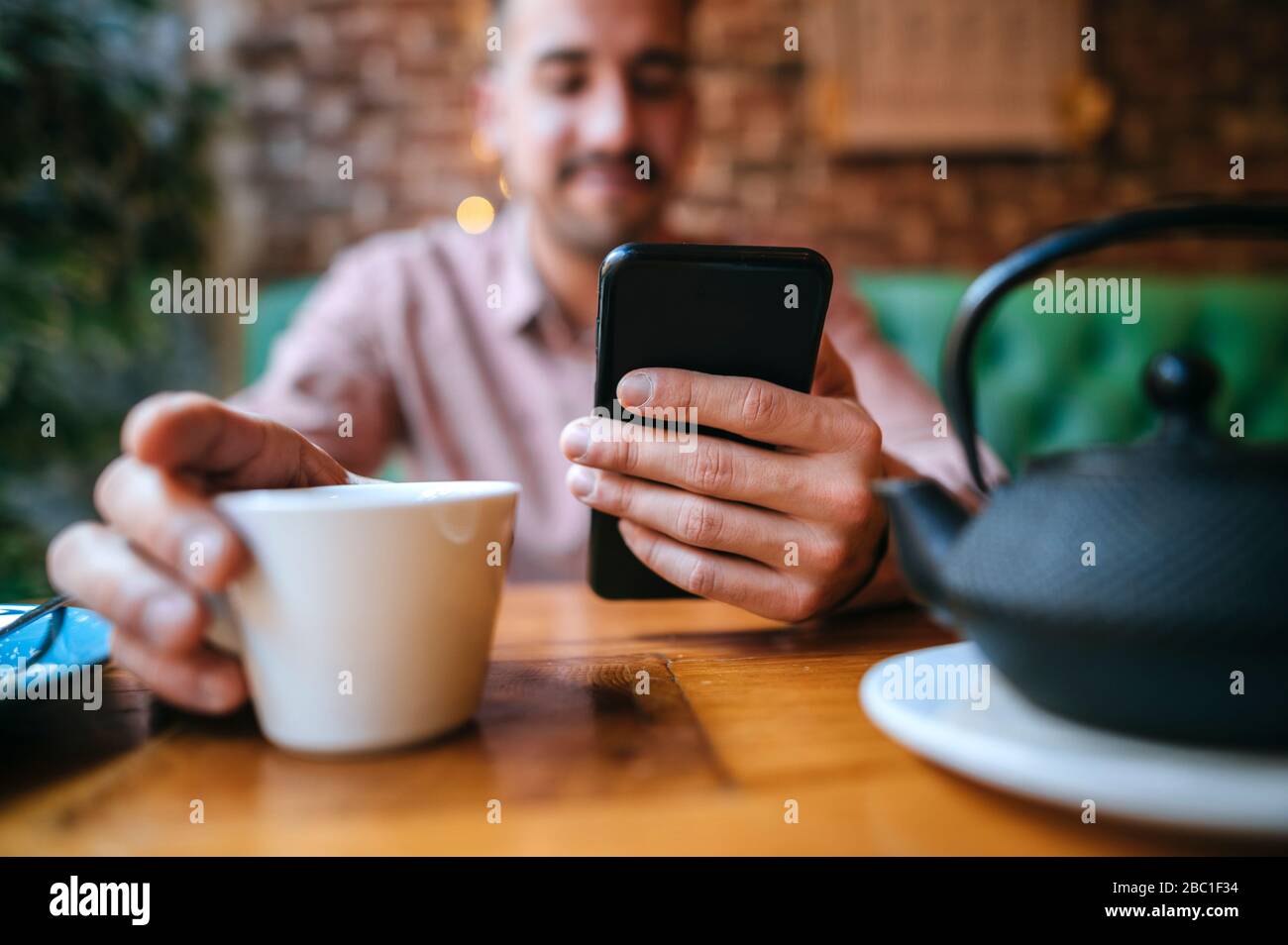 Primo piano di un uomo in un caffè con tazza da tè e telefono cellulare Foto Stock