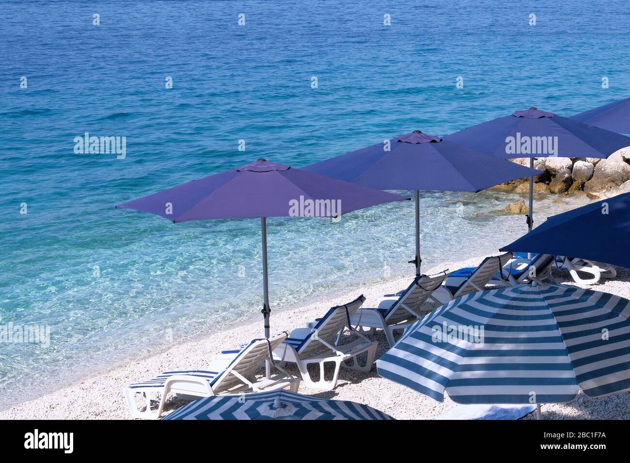 Ombrelloni e sedie a sdraio blu per il relax in una località balneare. Vacanze estive e viaggi per mare. Servizio a pagamento su spiagge confortevoli. Сopy spazio per il testo Foto Stock