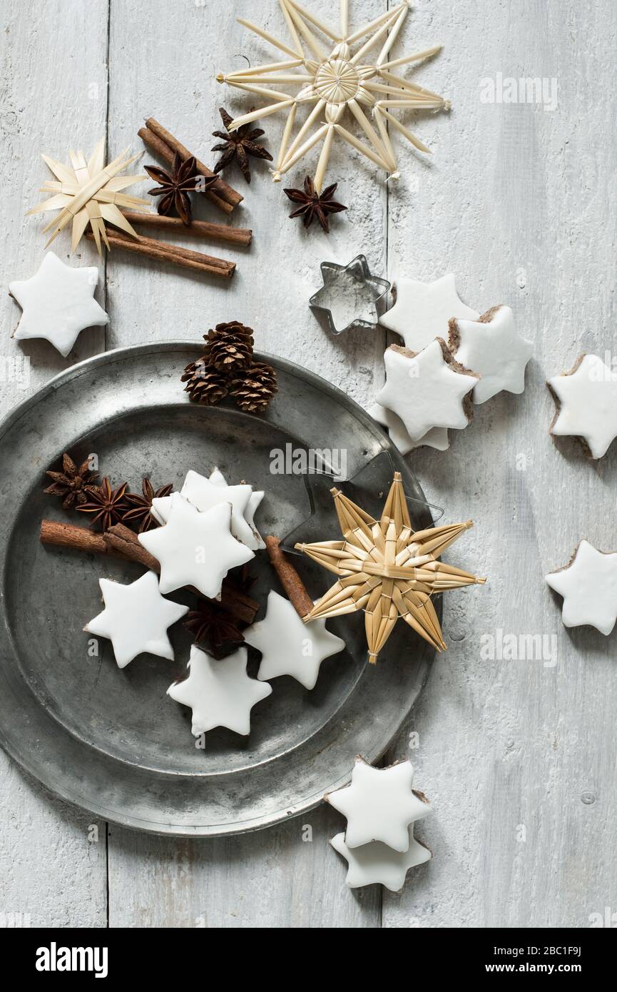 Biscotti a forma di stella, bastoncini di cannella, coni di pino, tagliatubi, piatto di peltro, anice stellato e decorazioni natalizie in paglia Foto Stock