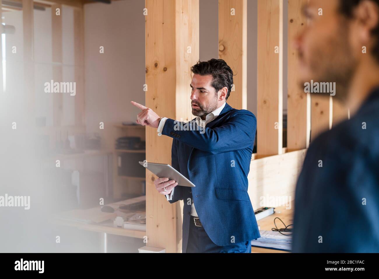 Uomo d'affari che tiene il tablet puntando il dito in un ufficio open-space in legno Foto Stock