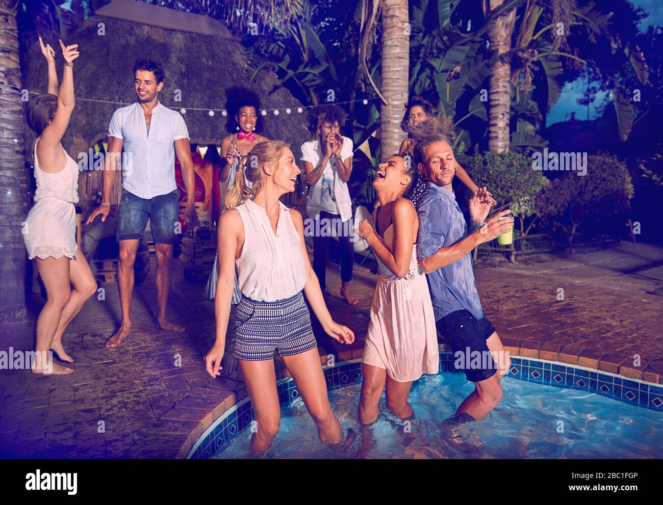 I giovani amici ballano e si appendono fuori alla festa estiva a bordo piscina di notte Foto Stock