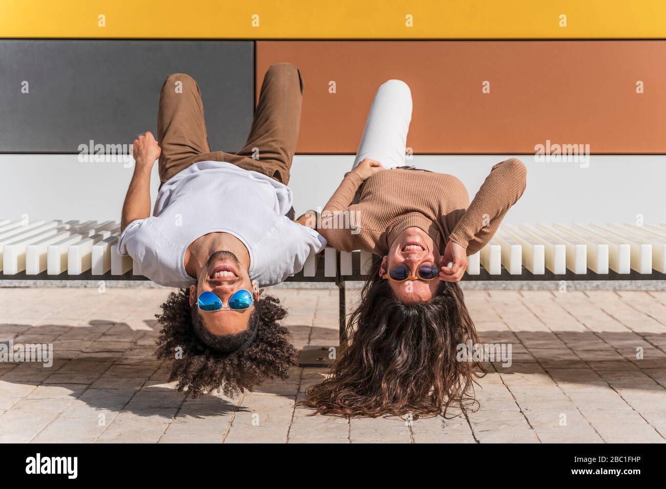 Coppia con occhiali da sole, relax su panchina, sdraiato sul retro, teste appese giù Foto Stock