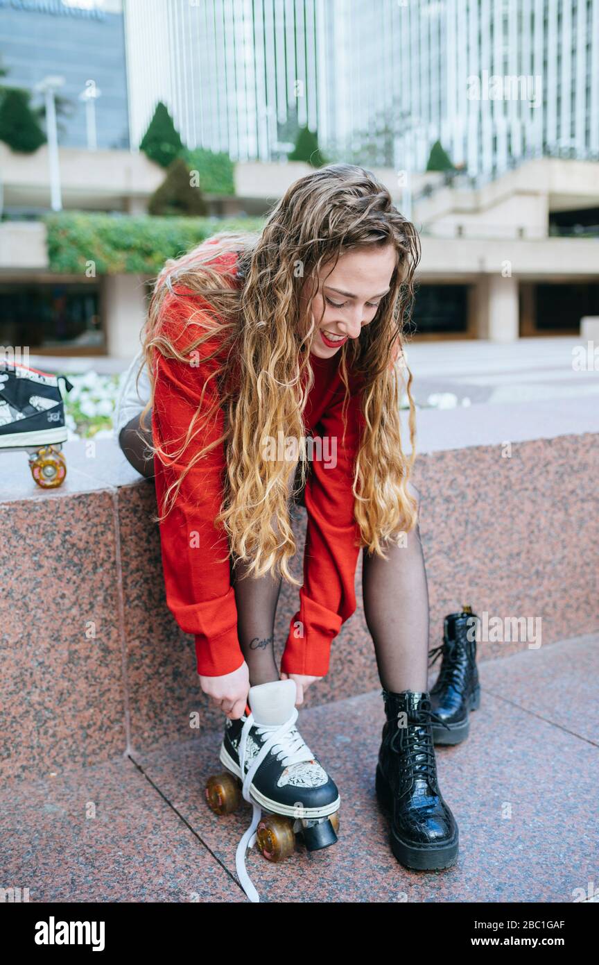 Giovane donna che mette su pattini a rotelle in città Foto Stock