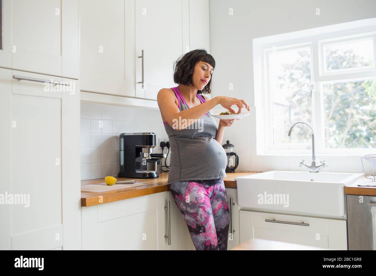 Donna incinta mangiare in cucina Foto Stock