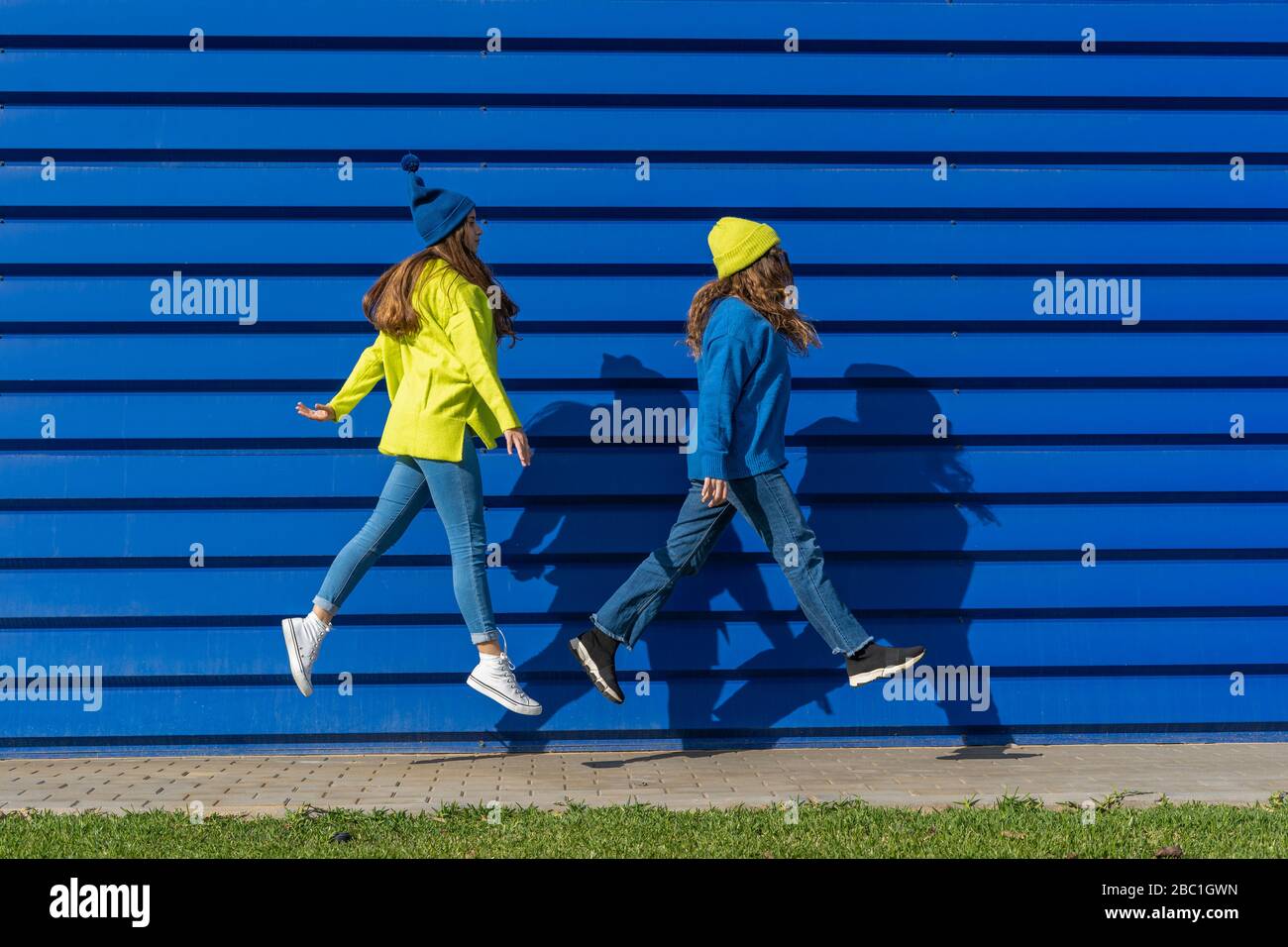 Due ragazze adolescenti che indossano abiti abbinati che saltano in aria di fronte a sfondo blu Foto Stock