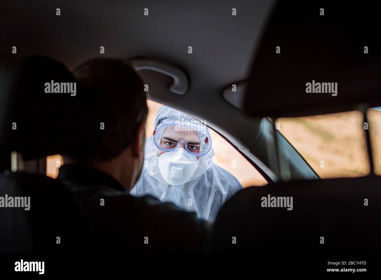 Uomo che indossa indumenti protettivi per controllare l'uomo anziano in auto Foto Stock