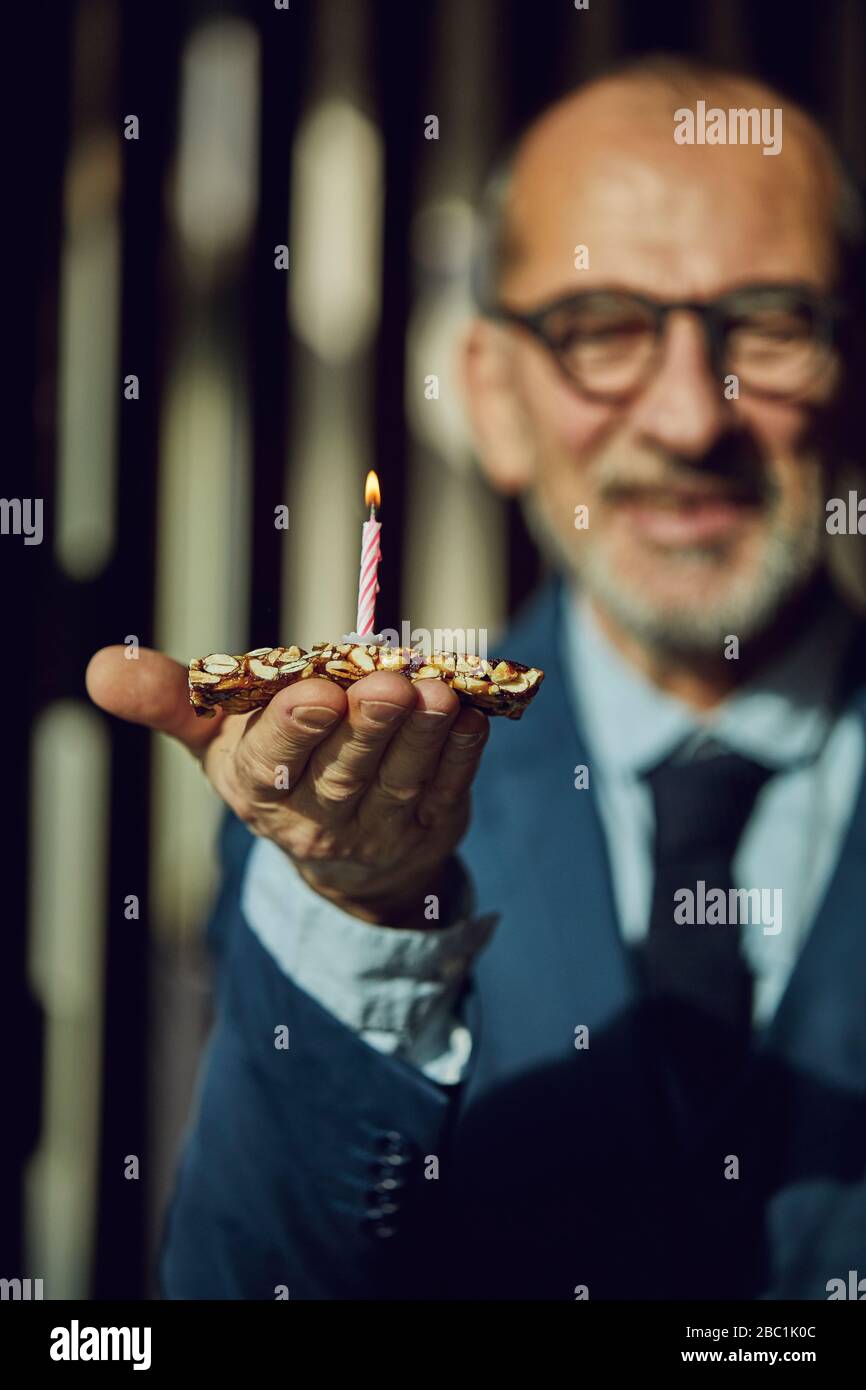 Uomo d'affari senior che tiene bar alla granola con candela di compleanno bruciante Foto Stock