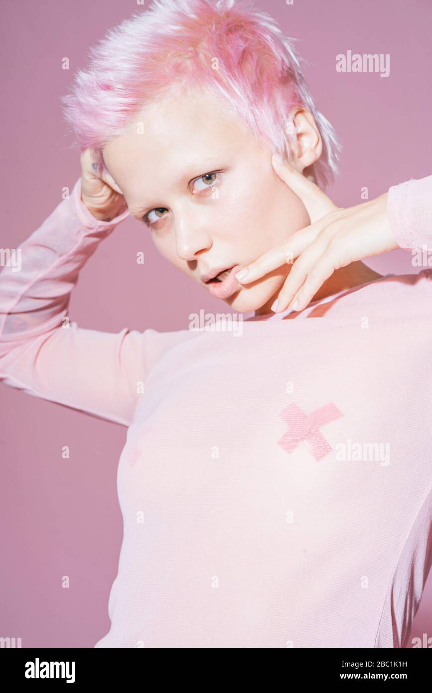 Ritratto di giovane donna con capelli rosa corti con top rosa davanti a fondo rosa Foto Stock