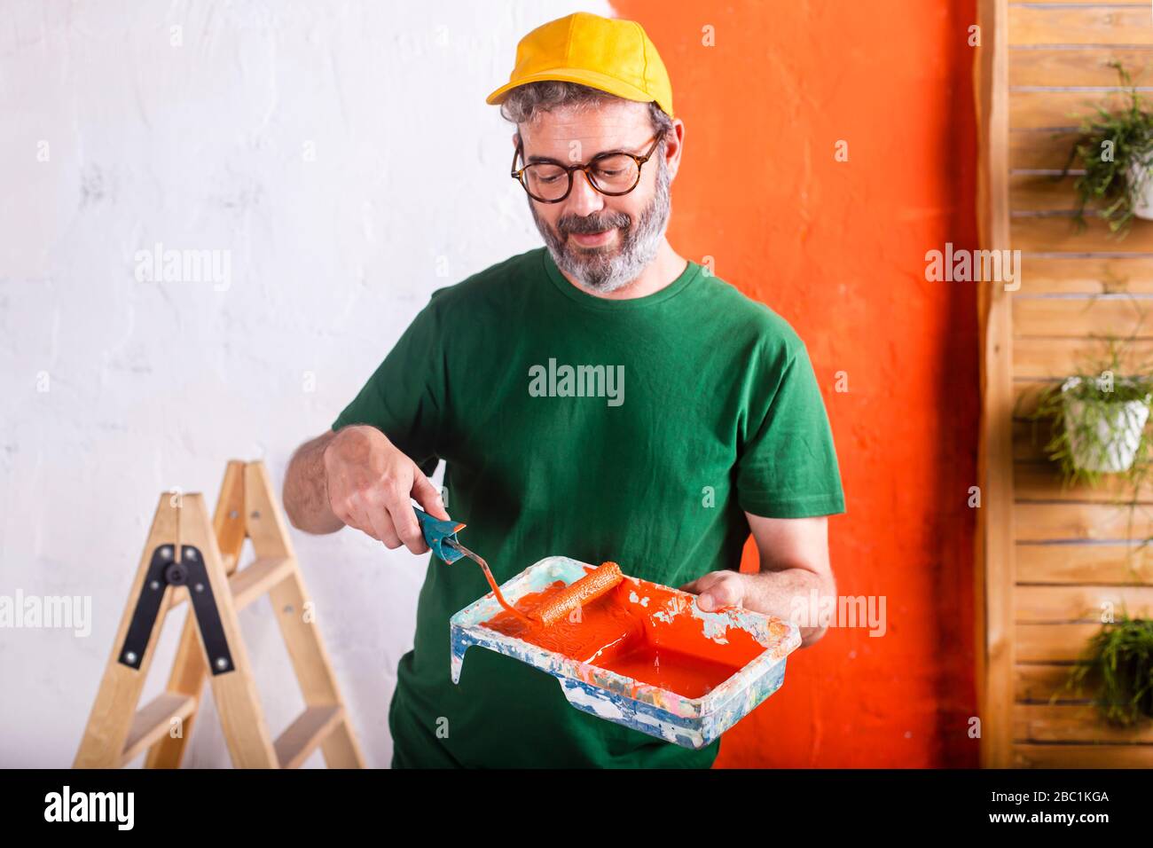 Uomo sorridente che tiene vassoio di vernice con vernice arancione Foto Stock
