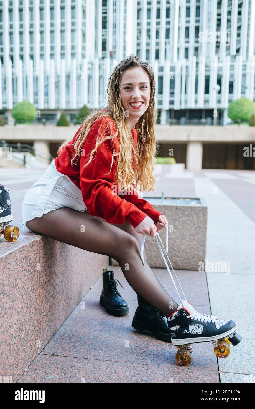 Ritratto di giovane donna felice che mette su pattini a rotelle nella città Foto Stock