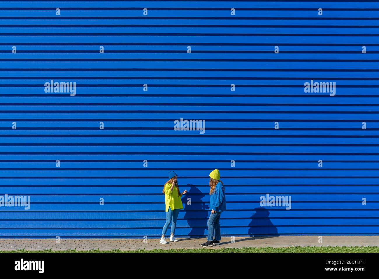 Due ragazze adolescenti che indossano abiti corrispondenti in piedi di fronte a sfondo blu Foto Stock