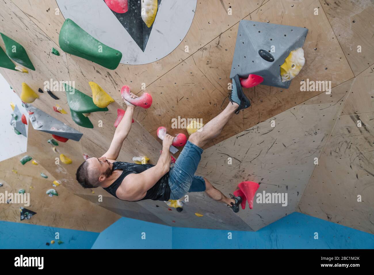 Uomo bouldering in palestra di arrampicata Foto Stock