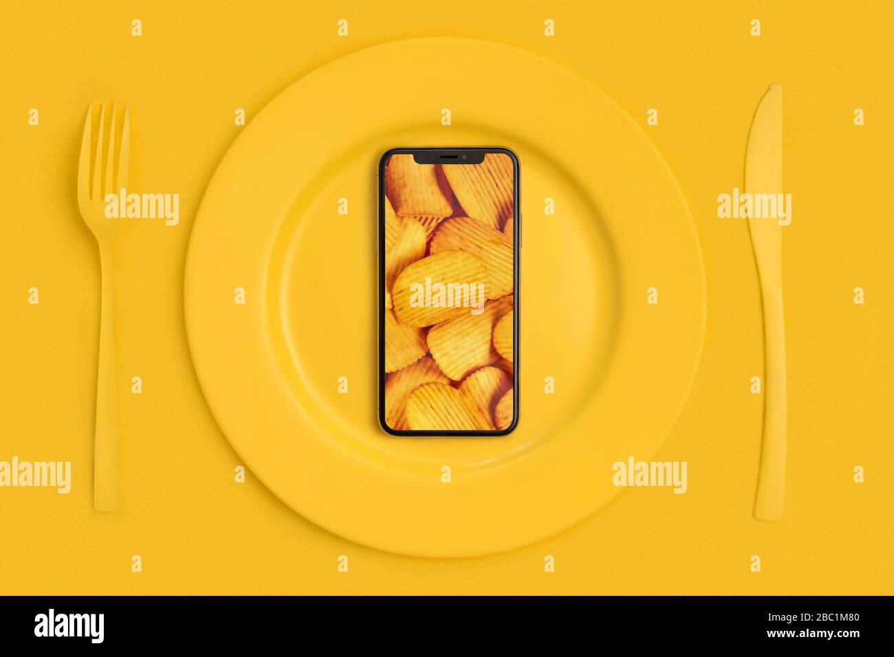 Ordinare cibo online, consegna cibo. Chiama e porta il cibo a casa. Smartphone con chip sullo schermo, sdraiato su una piastra, un coltello e una forcella. Giallo. La vista Foto Stock