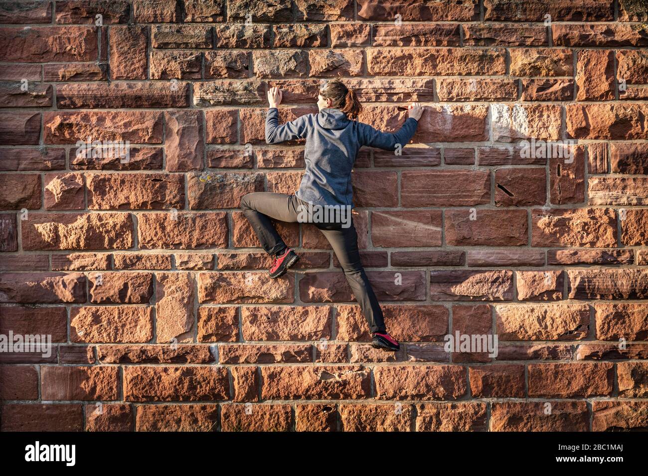 Donna che sale su muro di mattoni di arenaria Foto Stock