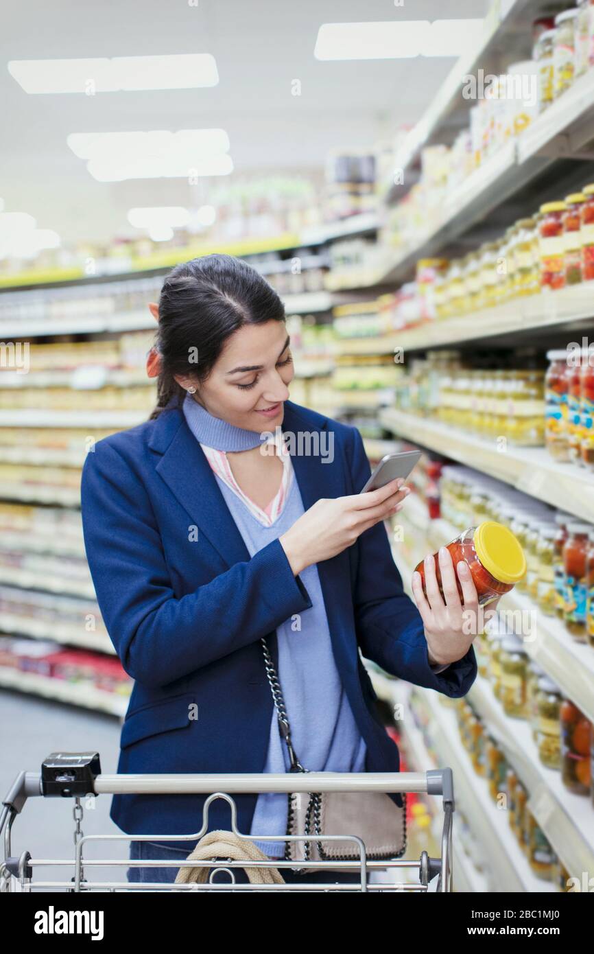 Donna con etichetta scansione smartphone sul vaso in supermercato Foto Stock