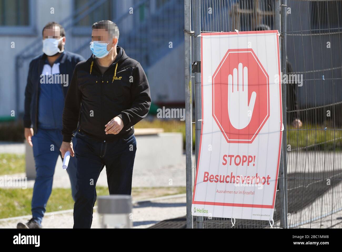 Monaco, Germania. 02nd Apr, 2020. Troppe infezioni da corona: Muenchner Helios Klinik cede le operazioni quotidiane. A causa di un gran numero di infezioni da corona tra pazienti e dipendenti, il Muenchner Klinik cede temporaneamente le normali operazioni ospedaliere. Anche la sala d'emergenza è interessata. Questo è il modo in cui le catene di infezione dovrebbero essere rotte. Due uomini escono dalla clinica con una maschera protettiva e una maschera facciale e passano un segno STOP! BESUCHSV Amburgo HamburgERBOT il 2nd aprile 2020. | utilizzo credito mondiale: dpa/Alamy Live News Foto Stock